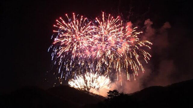 Fireworks exploding over mountain silhouettes in the dark night sky