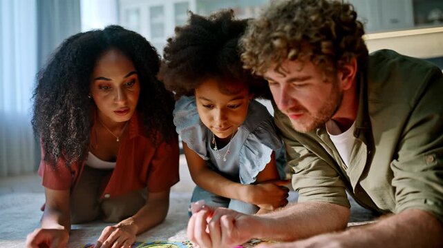 Little girl solving jigsaw puzzle with mom dad. Closeup hands living room floor.