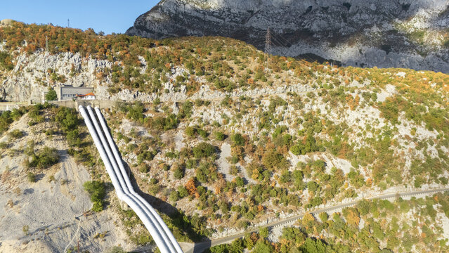 Aerial view of large industrial water pipelines running down a rocky mountainside with autumn foliage and power lines in Danilovgrad Municipal, Montenegro.