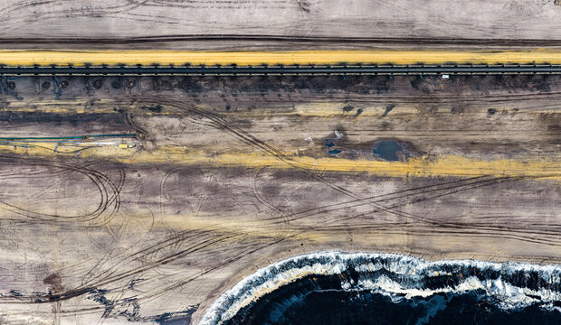 Aerial view of the Garzweiler surface mine featuring long conveyor belts, tire tracks across the excavated terrain, and coal deposits in Juchen, North Rhine-Westphalia, Germany.