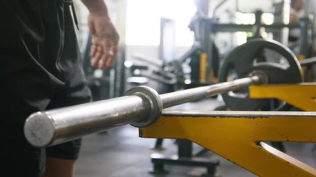 A close up shot of a weight plate is added to a barbell before performing resistance weight training or a workout, with a modern gymnasium visible in the background. Fitness, physical exercise concept
