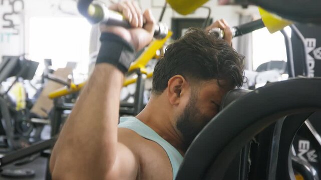 Young Indian Asian fit muscular man using a lat pulldown machine to perform a resistance weight training exercise targeting the back and shoulders in modern gym. Fitness, workout, bodybuilding concept
