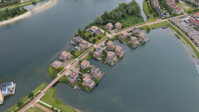 Aerial view of modern residential houses situated on a peninsula surrounded by water in a planned neighborhood with green spaces and paved paths in Houten, Utrecht, Netherlands.