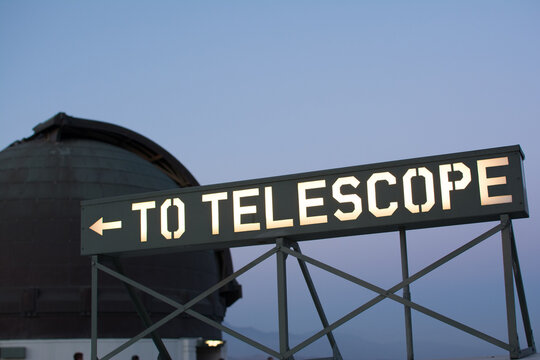 View of the illuminated TO TELESCOPE directional sign with the iconic observatory dome in the background at dusk in Los Angeles, California, United States.