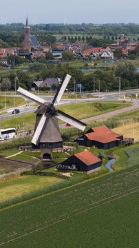 Aerial view of Bovenmolen E windmill surrounded by lush green fields and rural landscape with the village of Schermerhorn in the background in Schermerhorn, Noord-Holland, Netherlands.