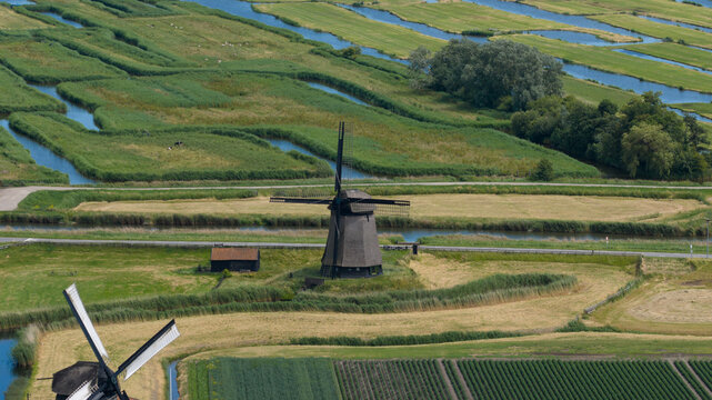Aerial view of Bovenmolen E windmill surrounded by lush green fields, winding canals, and agricultural land in Schermerhorn, Noord-Holland, Netherlands.