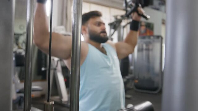 Low angle view of a young Indian Asian fit, muscular man performs a standing cable chest fly exercise during a resistance training session in a modern gym. Fitness, weight training workout concept
