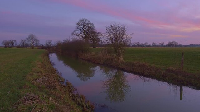 View along a ditch to the silhouettes of non-leafy trees at sunset, Kirchlinteln, Verden, Aller Leine Valley, Lower Saxony, Germany