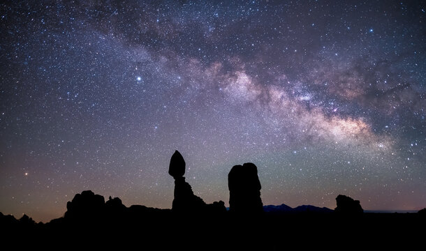 View of the iconic Balanced Rock formation silhouetted against the vibrant Milky Way galaxy and a star-filled night sky in Arches National Park, Grand County, Utah, United States.