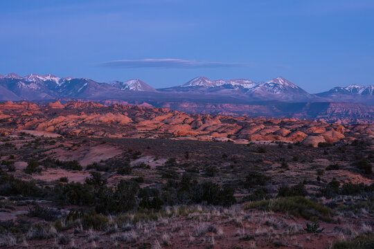 View of Arches National Park with snow-capped La Sal Mountains in the distance under a twilight sky in Grand County, Utah, United States.