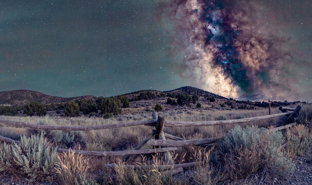 View of the historic Pony Express Trail at Lookout Pass with an ancient wooden fence under the vibrant Milky Way galaxy rising above the desert hills in Dugway, Utah, United States.