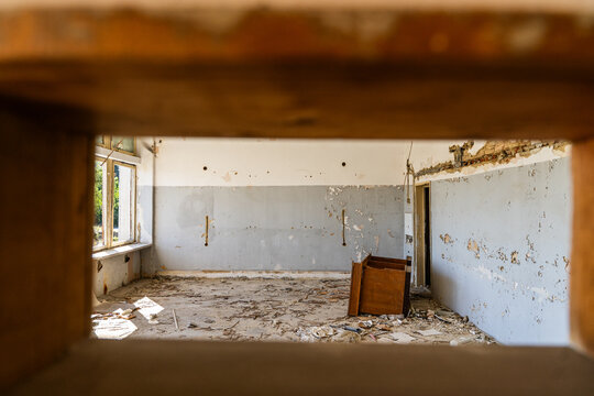 View of an abandoned room with peeling paint on the walls, scattered debris on the floor, and a wooden cabinet in Devnya, Varna, Bulgaria.