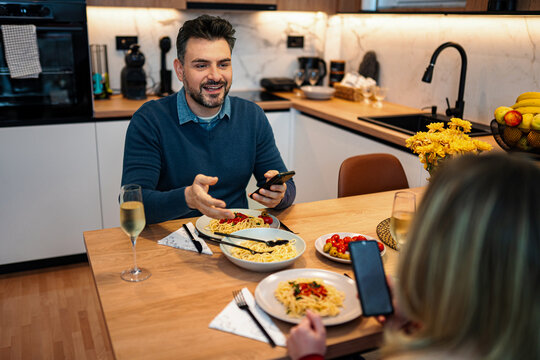 Man talking to woman phubbing during dinner at home kitchen