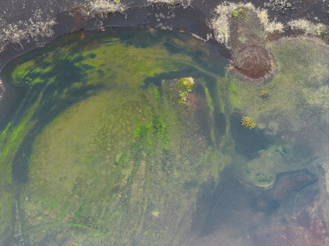 Aerial view of a geothermal pond with vibrant green algae and dark volcanic rock formations in the rugged landscape of Grindavik, Grindavikurbaer, Iceland.
