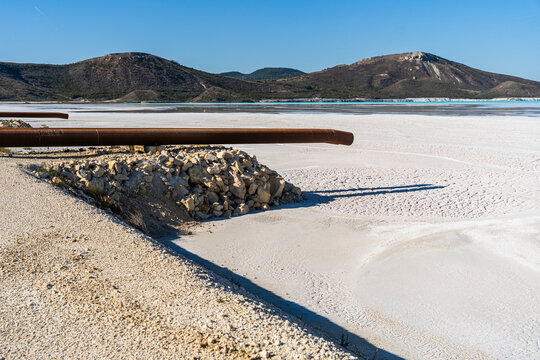 View of the Tailings Storage Facility with a large rusty pipe resting on a pile of rocks over a vast white sediment basin in Padina, Varna, Bulgaria.