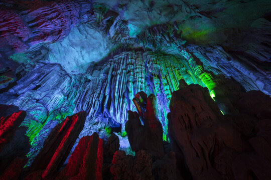View of illuminated stalactites and stalagmites inside a cave with vibrant blue, green, and red lighting in Yangshuo, Guangxi, China.