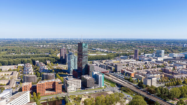 Aerial view of the modern skyline of Almere, featuring the World Trade Center tower, office buildings, train station tracks, and green urban surroundings in Almere, Flevoland, Netherlands.