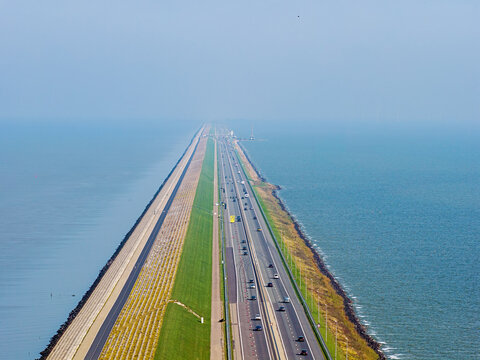 Aerial view of the Afsluitdijk causeway and Stevinsluis complex, featuring a multi-lane highway stretching across the water with green embankments in Den Oever, Noord-Holland, Netherlands.