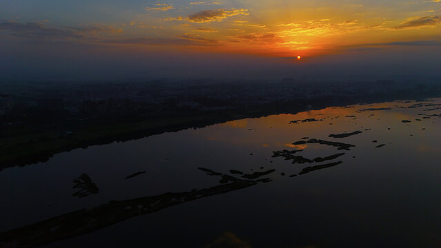 Aerial view of the Tapi River at sunset, with golden light reflecting on the water and dark silhouettes of river islands in Surat, Gujarat, India.
