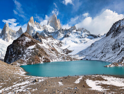 View of Laguna de los Tres with the snow-capped Mount Fitz Roy in the background, featuring a turquoise glacial lake, rocky shoreline, and hikers in El Chalten, Santa Cruz Province, Argentina.