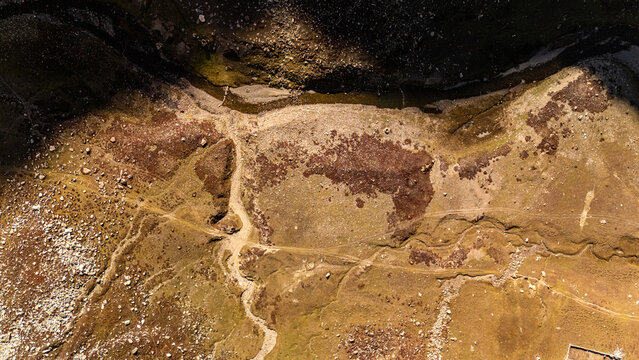 Aerial view of the rugged terrain of Supat Valley, featuring rocky ground, winding paths, and sparse vegetation under bright sunlight Kohistan, Khyber Pakhtunkhwa, Pakistan.