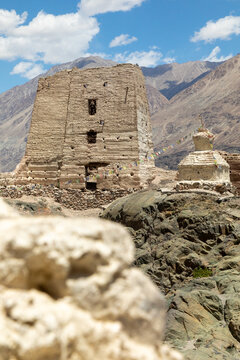 View of the ancient mud-brick structure and stupa of Charasa Gonpa adorned with prayer flags against a backdrop of rugged mountains in Charasa, Ladakh, India.