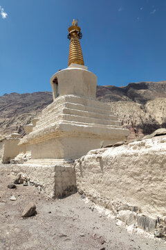 View of the white stupa at Charasa Gonpa with a golden spire set against arid mountains and a clear blue sky in Charasa, Ladakh, India.