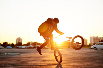 Naklejka premium City, skill and sunset with man on bicycle for adrenaline, exercise or extreme sports outdoor. BMX, flare and training with bike rider in parking lot of urban town for action, balance or practice