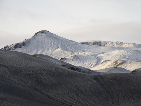 View of the snow-covered volcanic mountains of Landmannalaugar in the Icelandic highlands, featuring dark volcanic soil and soft light in Vik, Myrdalshreppur, Iceland.