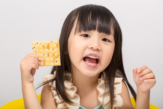 Cute little Asian girl eating a crispy cracker with mouth wide open, hungry child snacking