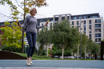 Fototapeta premium Happy senior woman exercising jumping rope outdoor