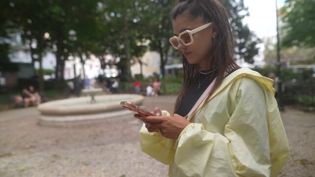 Woman using her smartphone beneath leafy trees in a city park