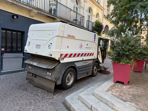 A white and gray street sweeper beside large planted containers on a cobblestone street - Rouen, France - September 6, 2026