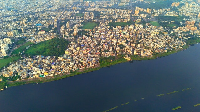 Aerial view of the dense urban landscape of Surat along the Tapi River, featuring a mix of residential buildings, green spaces, and city infrastructure in Surat, Gujarat, India.