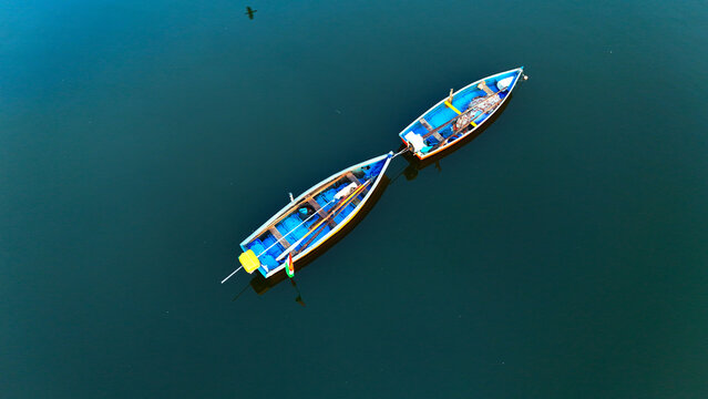 Aerial view of two small blue fishing boats floating on the calm dark water of the Tapi River in Surat, Gujarat, India.