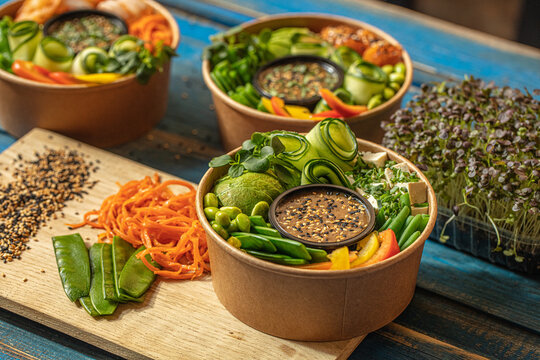 View of three bowls of fresh poke salad featuring avocado, cucumber, edamame, tofu, and sesame dressing on a wooden board in Latvia.