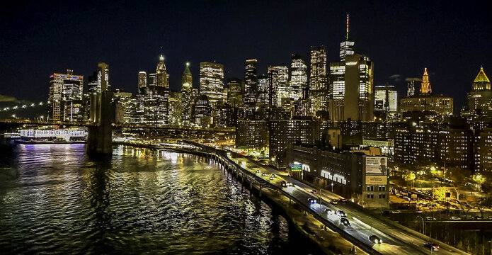 Aerial view of Brooklyn Bridge and Lower Manhattan skyline at night with illuminated skyscrapers and traffic on the FDR Drive New York, New York, United States.
