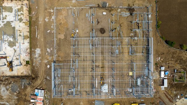 Aerial view of a warehouse construction site featuring a steel frame structure, heavy machinery, and surrounding earthworks in Bhiwandi, Maharashtra, India.