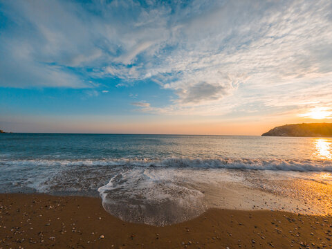 View of the Adriatic Sea at sunset with gentle waves washing onto the sandy beach in Montenegro.