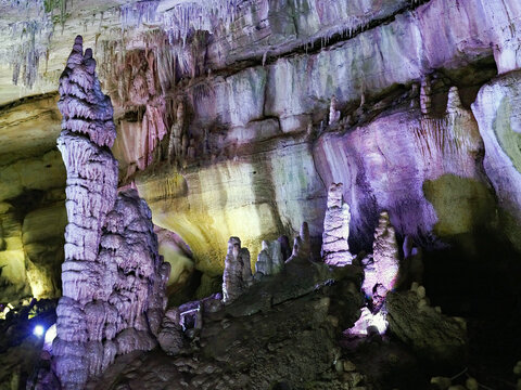 Towering stalagmites, columns, and delicate drapery formations are illuminated by colorful theatrical lighting within a subterranean karst cave near Kutaisi in the Imereti region of Georgia