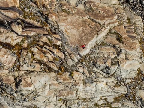 Aerial view of a person lying on the textured rock formations of the Aletsch Glacier with visible geological layers and patches of moss in Fieschertal, Valais, Switzerland.