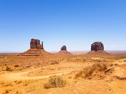 View of the iconic red sandstone buttes of Oljato-Monument Valley rising from the desert floor under a clear blue sky in Oljato-Monument Valley, Arizona, United States.