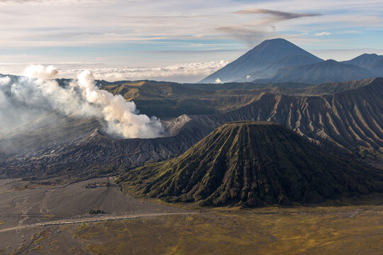 Mount Bromo volcano at sunrise, viewed from King Kong viewpoint in Bromo Tengger Semeru National Park, East Java, Indonesia. Active crater smoke, Mount Semeru cone, clouds, and vast ash plain.