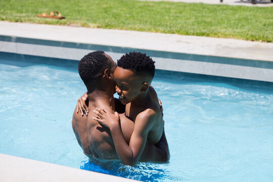 African American father and son standing shirtless in backyard pool holding smiling