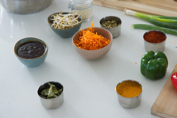 Pink ribbed bowl holding shredded carrots is sitting on white countertop near teal bowls and spices © WavebreakMediaMicro