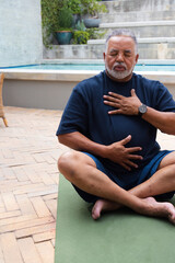Fototapeta premium Senior African American man sitting on green yoga mat beside pool wearing navy T-shirt and watch