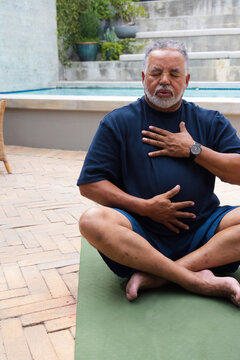 Senior African American man sitting on green yoga mat beside pool wearing navy T-shirt and watch
