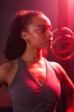 African American woman in her twenties training in fitness studio wearing grey tank top, gym rings