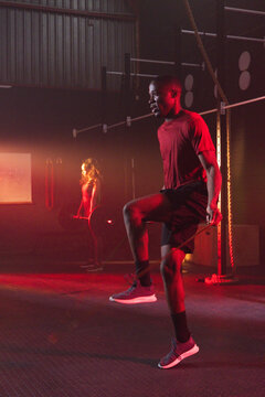 African American duo training in red-lit gym, man jumping rope, woman holding weight in red tops