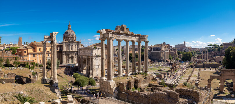 View of the Roman Forum with the Temple of Saturn columns and the Arch of Septimius Severus under a clear blue sky in Rome, Lazio, Italy.